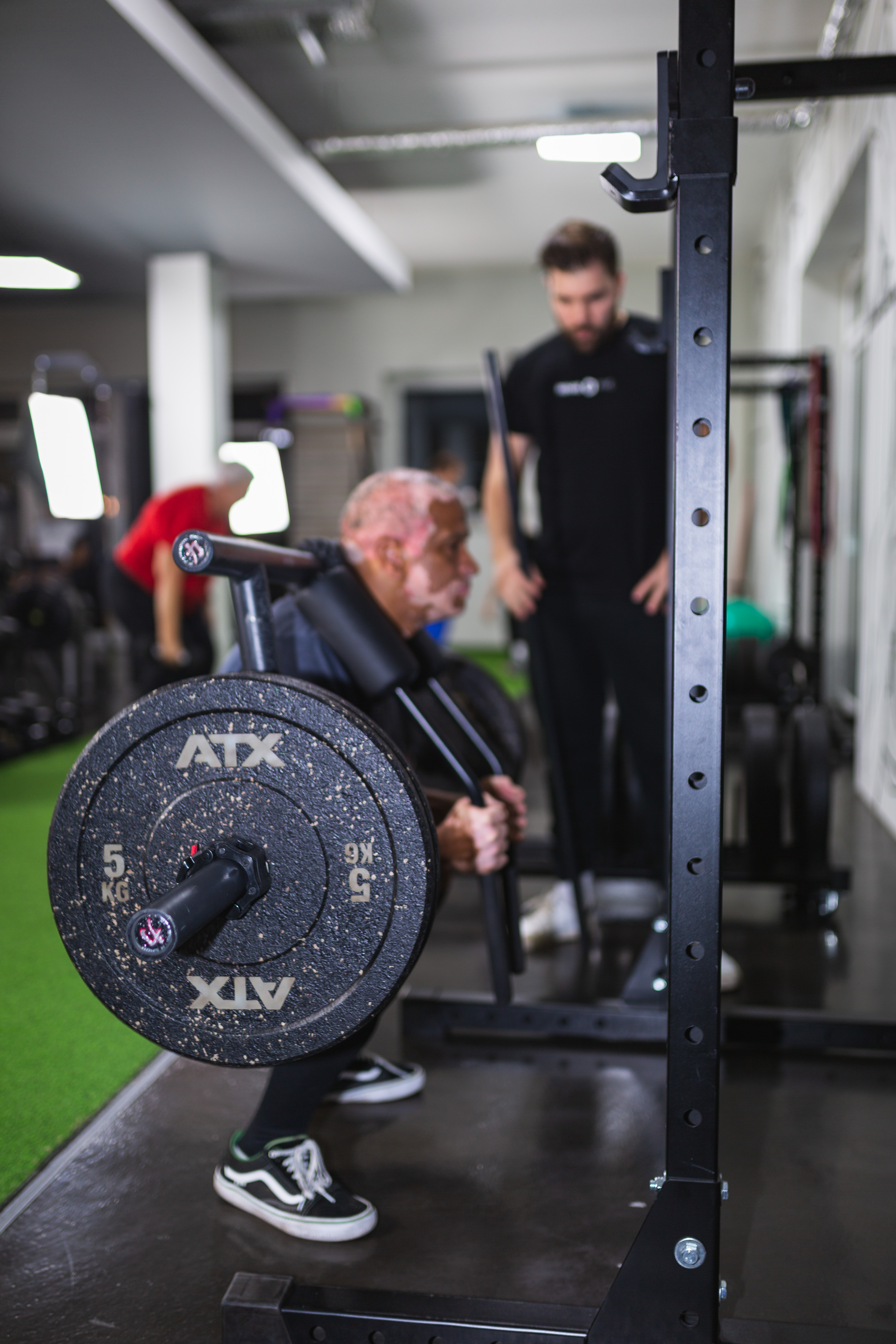 Senior beim Squat-Training mit Rack — Coach im Hintergrund