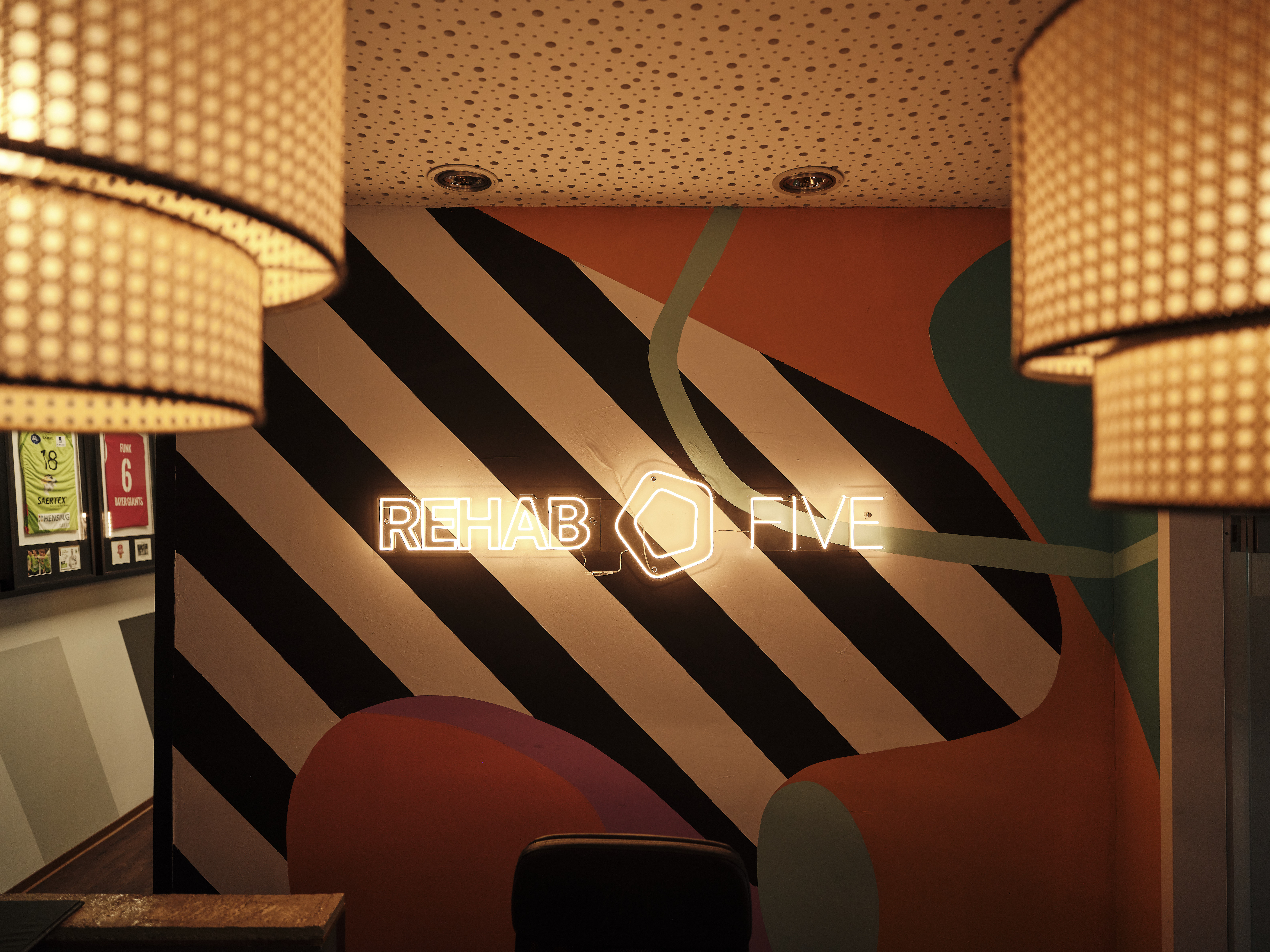 Empfang REHAB FIVE Scharnhorststraße — Logo in Neon vor schwarzem Streifen-Mural